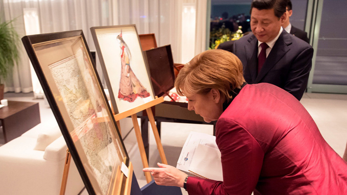  Món quà Thủ tướng Đức Angela Merkel tặng Chủ tịch Trung Quốc Tập Cận Bình hồi tuần trước khiến cư dân mạng Trung Quốc sôi sục, đặc biệt là khi ngay cả báo chí nước này cũng phản ứng rất lạ lùng!  Hồi tuần trước, Thủ tướng Đức Angela Merkel đã mời Chủ tịch Trung Quốc Tập Cận Bình ăn tối nhân chuyến thăm kéo dài 2 ngày của ông ở Đức và hai người tặng quà cho nhau. Bà Merkel tặng ông Tập một tấm bản đồ vẽ lãnh thổ Trung Quốc thời Càn Longdo nhà vẽ bản đồ người Pháp Jean-Baptiste Bourguignon d’ Anville thực hiện và in tại Đức năm 1735. Thủ tướng Đức tặng tấm bản đồ cổ vẽ lãnh thổ Trung Quốc cho Chủ tịch Tập Cận Bình. Ảnh: Time.  Thủ tướng Đức tặng tấm bản đồ cổ vẽ lãnh thổ Trung Quốc cho Chủ tịch Tập Cận Bình. Ảnh: Time.  Trên tấm bản đồ vẽ lãnh thổ Trung Quốc đầu tiên được xuất bản tại Đức này hoàn toàn không có sự hiện diện và vùng Tibet (Tây Tạng), Xinjiang (Tân Cương), Manchuria (Mãn Châu Lý). Các đảo Đài Loan và Hải Nam thì được vẽ bằng màu sắc khác. Tất nhiên tấm bản đồ cũng hoàn toàn không có quần đảo Hoàng Sa và Trường Sa của Việt Nam.  Điều bất ngờ là truyền thông Trung Quốc tỏ ra không đánh giá cao món quà của nữ Thủ tướng Đức. Tờ People's Daily thông tin rất chi tiết về chuyến đi của ông Tập Cận Bình, song lại lờ đi bất cứ thông tin nào về tấm bản đồ này. Kì lạ hơn là khi thông tin về tấm bản đồ này lan truyền tại Trung Quốc đại lục thì lại là một phiên bản hoàn toàn khác. Nhiều tờ báo Trung Quốc lại đăng tải một tấm bản đồ Trung Quốc do chuyên gia bản đồ người Anh John Dower in năm 1844 của nhà xuất bản Henry Teesdale & Co. tại London, với các lãnh thổ bao gồm Tây Tạng, Tân Cương, Mông Cổ và những vùng rộng lớn ở Siberia.Truyền thông Trung Quốc cũng không đả động gì tới thông tin sai lệch nghiêm trọng này!  Tuy nhiên không khó để các cư dân mạng nước này tìm ra món quà thực sự của Thủ tướng Đức khi hàng loạt báo chí phương Tây đều đăng tải về sự kiện này.  Một cư dân mạng gọi tấm bản đồ là một “cái tát” từ bà Merkel. “Chúng ta luôn nói những vùng đất đó là một phần của Trung Quốc từ thời cổ đại, thế nhưng bà Merkel lại nói rằng thậm chí tới thế kỉ 18 những khu vực đó vẫn không thuộc về Trung Quốc” – người này chỉ trích.  Một số ý kiến cho rằng món quà của bà Merkel rất ý nghĩa trong bối cảnh vấn đề khủng hoảng ở Ukraine đang nóng và tấm bản đồ chính là ngụ ý của Thủ tướng Đức nhằm nhắc nhở Trung Quốc về những vết thương trong quá khứ sau các cuộc bành trướng trước đây.  Tuy nhiên cũng cho ý kiến cho rằng không nên quá nhạy cảm về tấm bán đồ từ thế kỷ 18 của d’Anville và coi đó là thông điệp về Tây Tạng hoặc Tân Cương.  Tờ Time bình luận rằng có lẽ bản đồ không phải là một món quà hoàn hảo cho các vị nguyên thủ quốc gia.